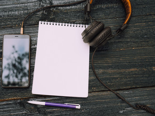 Headphones, smartphone and blank notebook on black wooden table