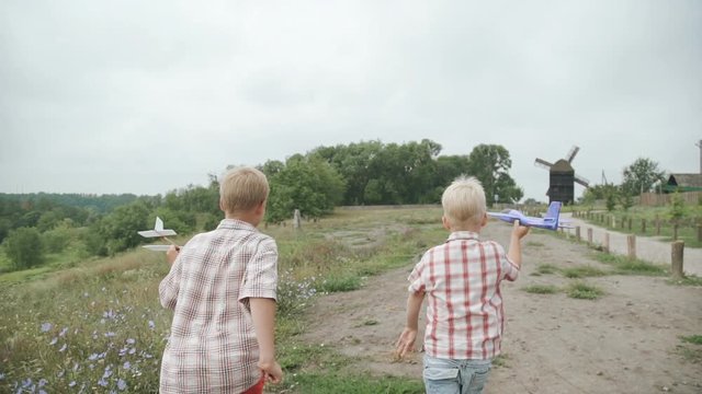 Two boys running with his airplanes in the park