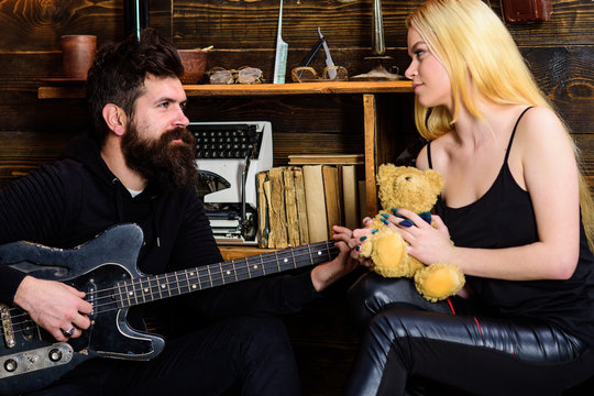 Couple in love on relaxed faces enjoy romantic atmosphere. Romantic date concept. Couple spend romantic evening, wooden interior background. Man play guitar while lady holds teddy bear in hands