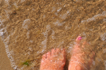 Feet in sea water. Women's feet on the sand.