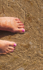 Feet in sea water. Women's feet on the sand.