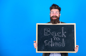 Teacher bearded man stands and holds blackboard with inscription back to school blue background. Teacher invites to continue studying. Continue your education with us. New semester in school