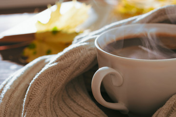 Cup of hot coffee among leaves and scarf