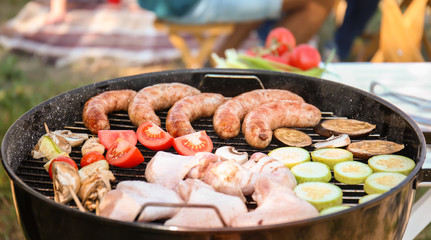 Meat and vegetables on modern barbecue grill with group of friends outdoors