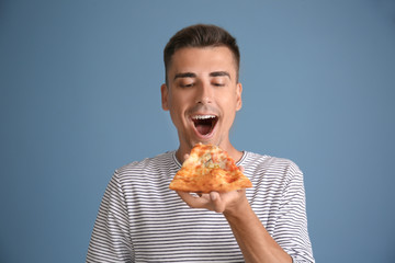 Handsome young man with delicious pizza on color background