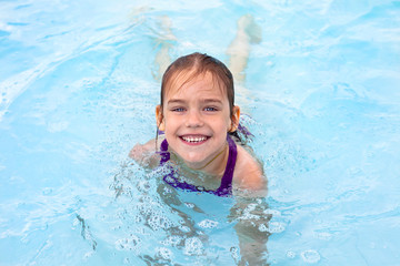 Fototapeta na wymiar A little girl swims in the pool, smiling looking at the camera.