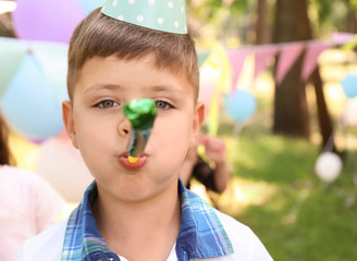 Cute little boy with party whistle celebrating birthday outdoors