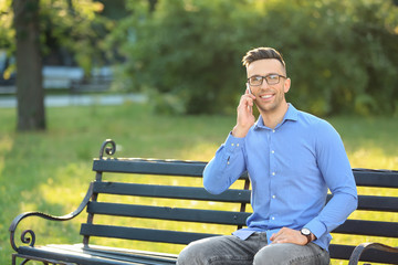 Handsome man talking on mobile phone while resting in green park