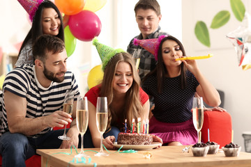 Young woman with tasty cake and her friends at birthday party indoors