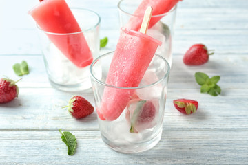 Glass with delicious strawberry popsicle on wooden table