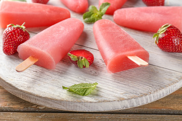 Delicious strawberry popsicles with berries on wooden board