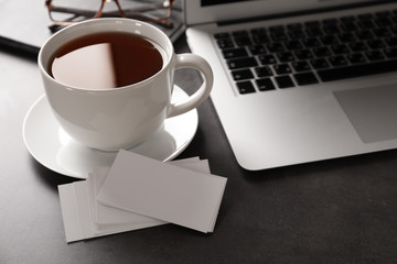 Obraz na płótnie Canvas Blank business cards with laptop and cup of tea on grey table