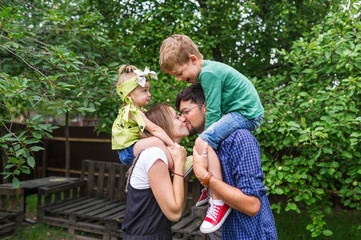 Cheerful family of four having fun at countryside. The father kisses mother.