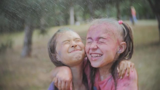 Two little girls smeared with colored powder Holi sprinkle water in the summer Park