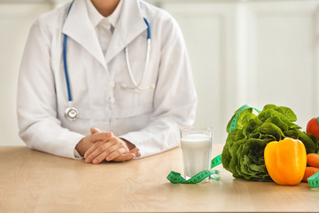 Female nutritionist sitting at table with vegetables and glass of milk in her office
