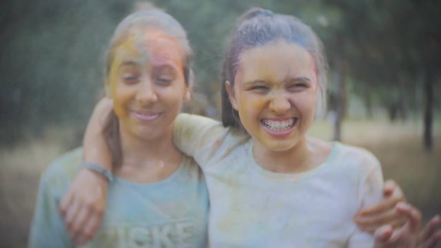 Two teenage girls smeared with colored powder Holi sprinkle water in the summer Park in Slow motion