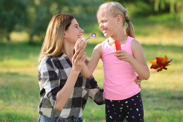 Obraz premium Woman and her daughter blowing soap bubbles in park