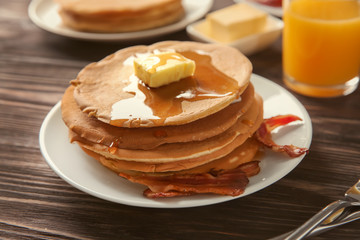 Plate with tasty pancakes and bacon on wooden table