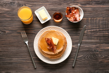 Plate with tasty pancakes and bacon on wooden table