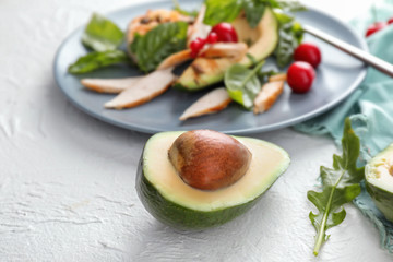 Half of ripe avocado near plate with salad on table