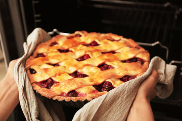 Woman taking freshly baked cherry pie out of oven, closeup