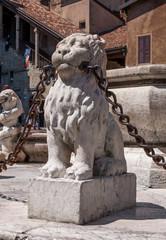 Lion stone statue with metal chain in the mouth, Bergamo town, Italy. Serves as a fencing fountain in the city square