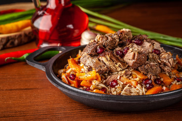 Uzbek traditional cuisine. Pilaf or plov with lamb, and red garnet, in an iron cast-iron frying pan kazan. Background image. Copy space, selective focus