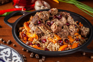 Uzbek traditional cuisine. Pilaf or plov with lamb, and red garnet, in an iron cast-iron frying pan kazan. Background image. Copy space, selective focus