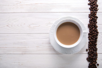   White cup of coffee with milk or tea with milk on white wooden background decorated with coffee beans. Copy space