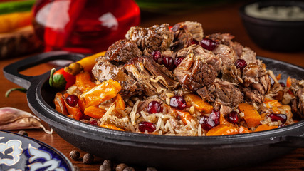Uzbek traditional cuisine. Pilaf or plov with lamb, and red garnet, in an iron cast-iron frying pan kazan. Background image. Copy space, selective focus