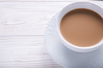   White cup of coffee with milk or tea with milk on white wooden background decorated with coffee beans. Copy space