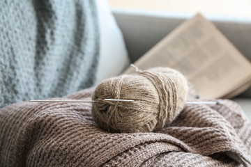 Fototapeta na wymiar Knitting yarn with clothes and needles on sofa