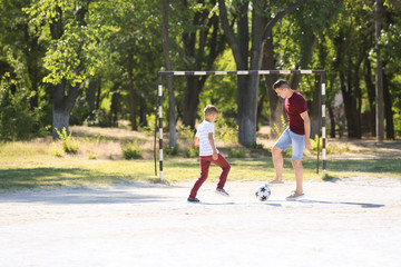 Little boy with his dad playing football on soccer pitch