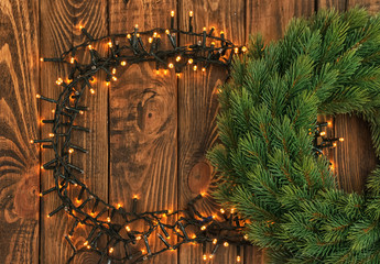 Frame made of beautiful bright Christmas lights and fir wreath on wooden background