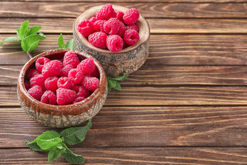 Bowls with delicious fresh ripe raspberries on wooden background