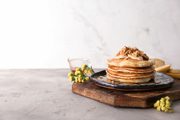 Wooden board with tasty pancakes, sliced banana and walnuts on grey table