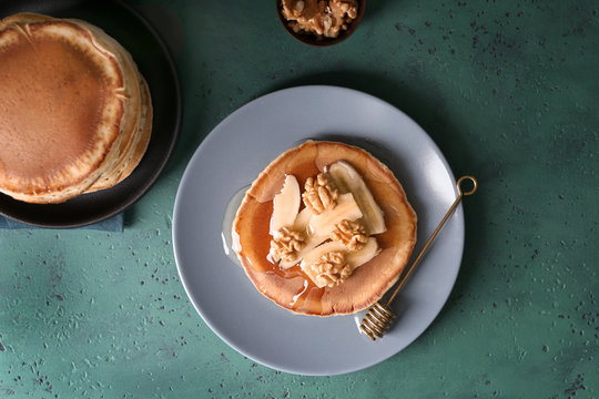 Plate with tasty pancake, sliced banana and walnuts on color textured background
