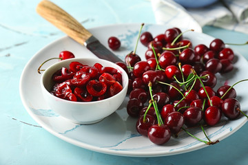 Bowl and plate with ripe cherries on color table