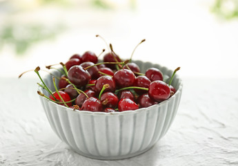 Bowl with ripe cherries on light table