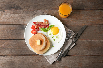 Tasty pancakes with fried egg and bacon on wooden table