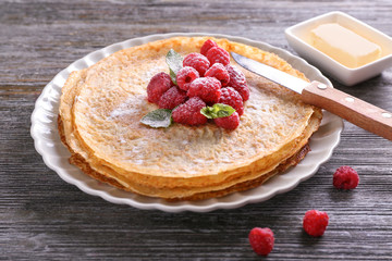 Plate with delicious thin pancakes and raspberries on wooden table