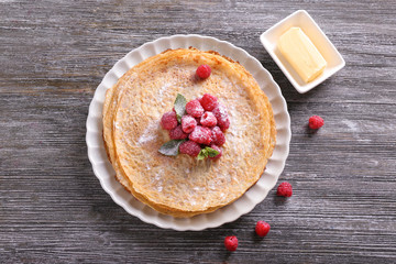 Plate with delicious thin pancakes and raspberries on wooden table