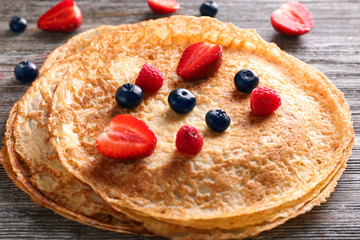 Delicious thin pancakes with berries on wooden table