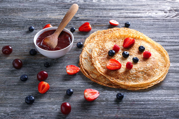 Delicious thin pancakes with berries and jam on wooden table
