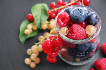 Glass jar with different ripe berries on dark table