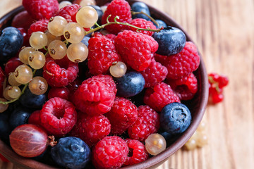 Bowl with different ripe berries on wooden table, closeup
