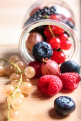 Overturned glass jar with different ripe berries on wooden table