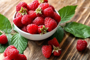 Bowl with ripe aromatic raspberries on wooden background
