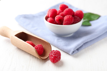 Bowl and scoop with ripe aromatic raspberries on white wooden table
