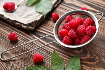 Sieve with ripe aromatic raspberries on wooden background